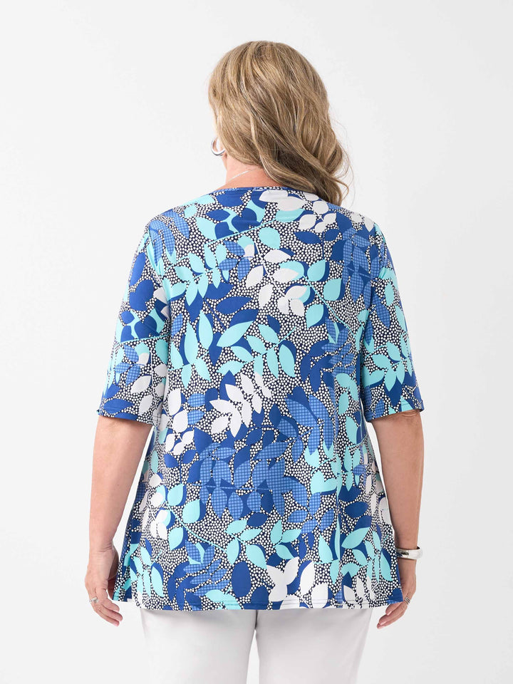 A woman viewed from the back wearing a short-sleeve top with a botanical leaf pattern, paired with white pants