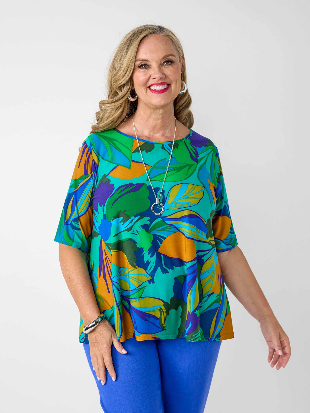 front view of model wearing a short-sleeve top with a bold tropical leaf print in green, blue, and orange