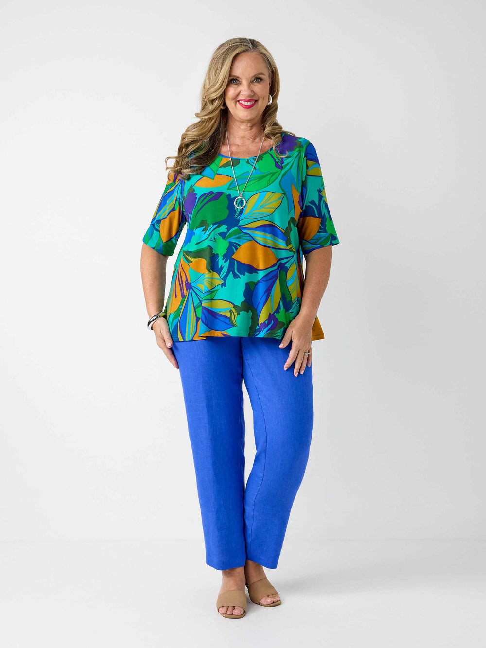 model wearing a short-sleeve top with a bold tropical leaf print in green, blue, and orange