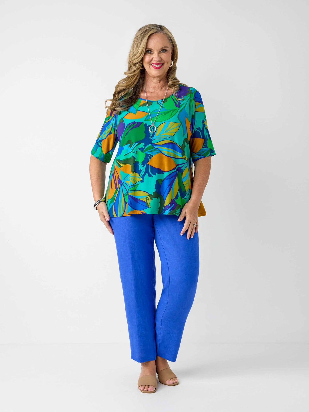 model wearing a short-sleeve top with a bold tropical leaf print in green, blue, and orange