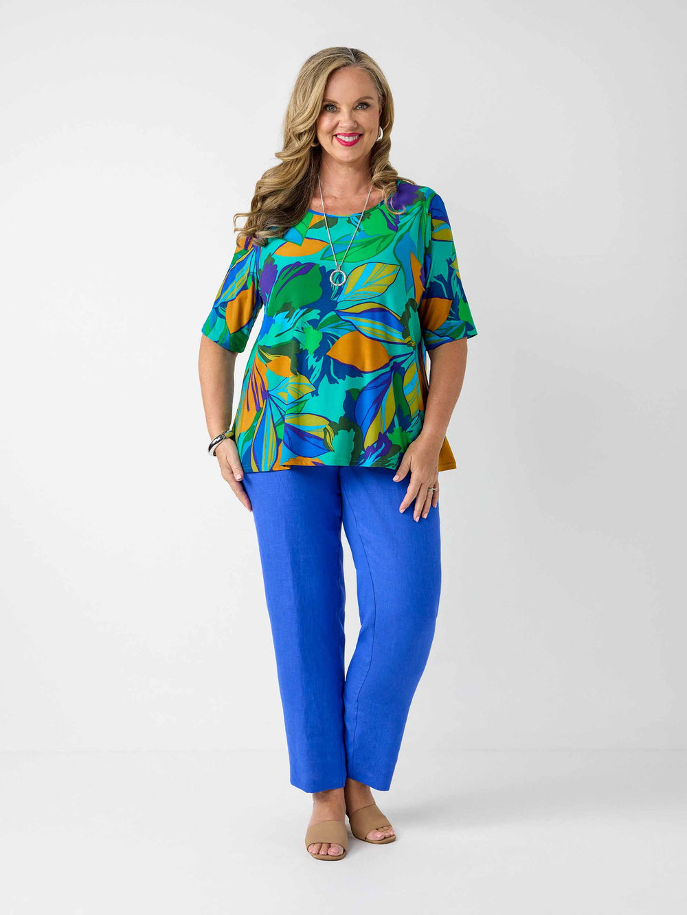 model wearing a short-sleeve top with a bold tropical leaf print in green, blue, and orange