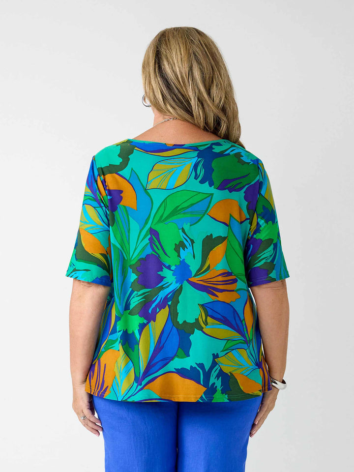 back view of model wearing a short-sleeve top with a bold tropical leaf print in green, blue, and orange