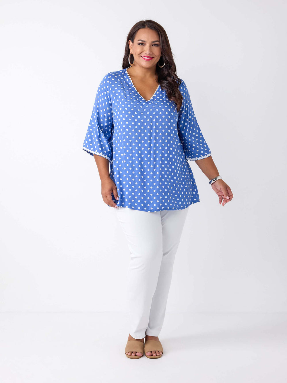 A woman wearing a blue top with white polka dots and ric rac trim details around the v-neckline and three-quarter sleeves