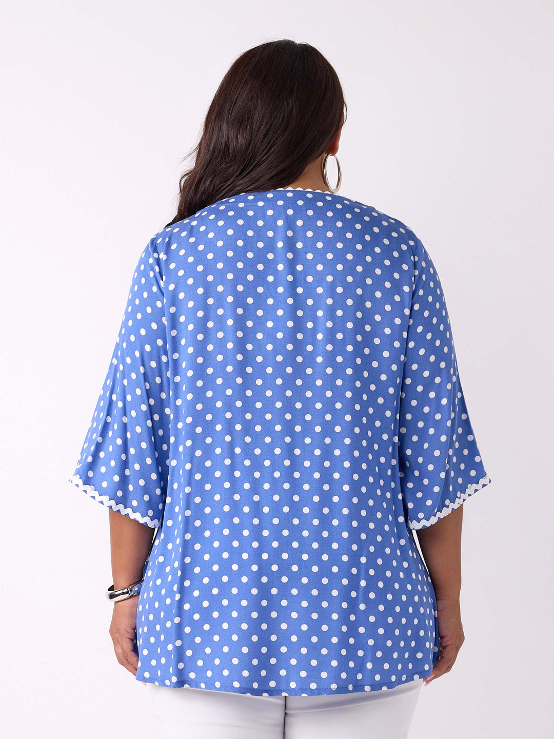 A woman wearing a blue top with white polka dots and ric rac trim details around the v-neckline and three-quarter sleeves
