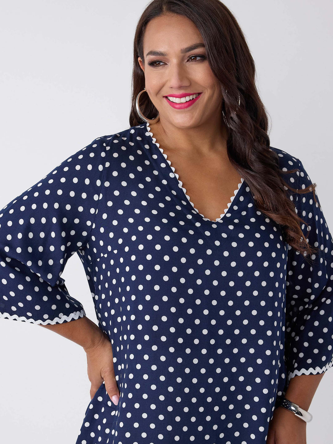 A woman wearing a navy blue V-neck top with white polka dots and ric rac trim on three-quarter sleeves and around neckline