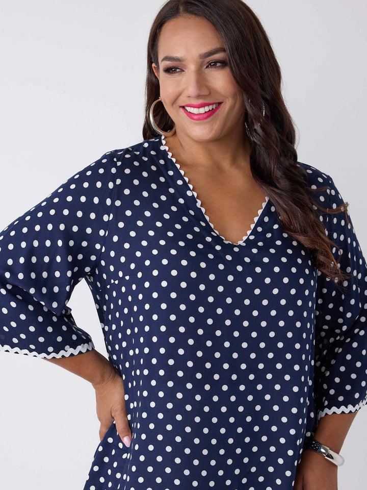 A woman wearing a navy blue V-neck top with white polka dots and ric rac trim on three-quarter sleeves and around neckline