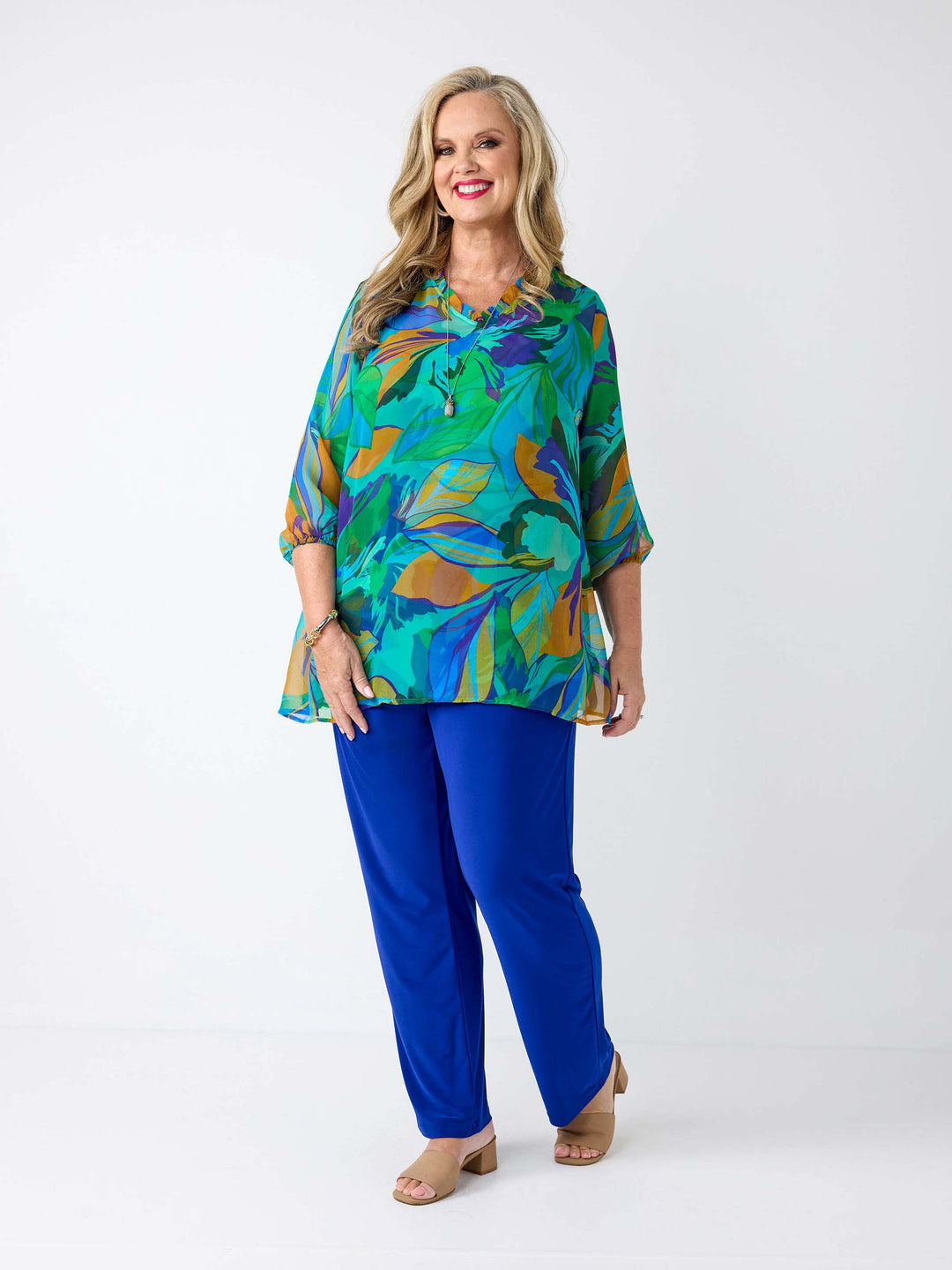 A woman wearing a vibrant, multicoloured abstract print georgette top with blue, green, orange, and purple tones, paired with bright blue pants