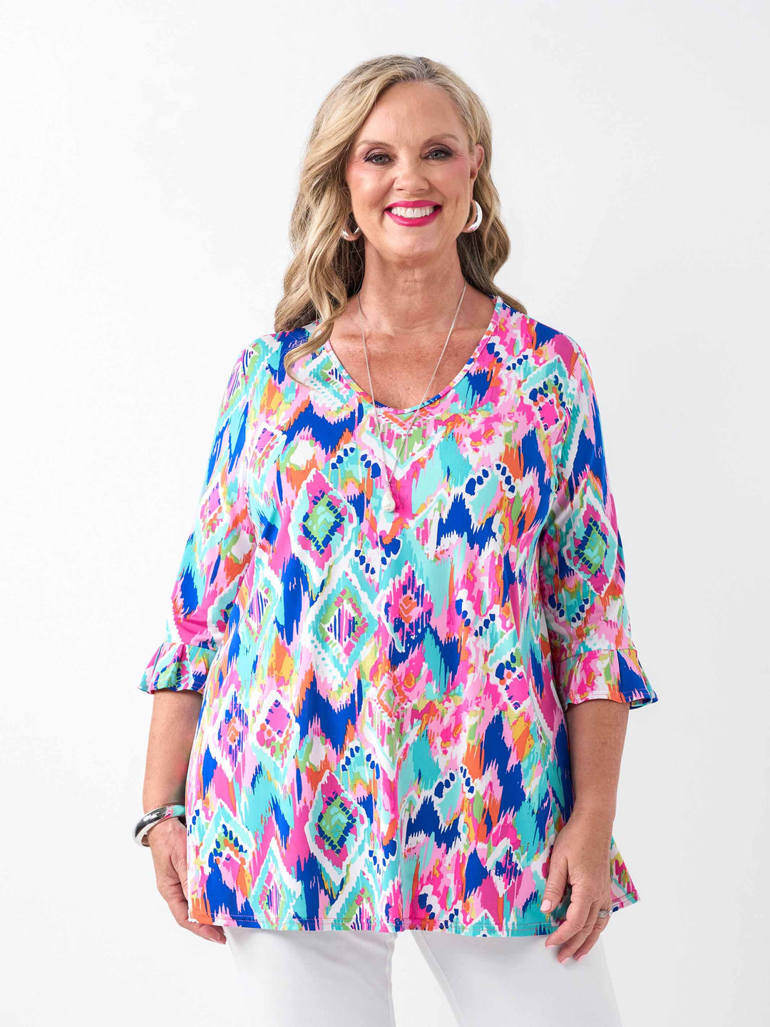 a woman wearing a v-neck frill sleeve summer top with vibrant and playful print, paired with white pant