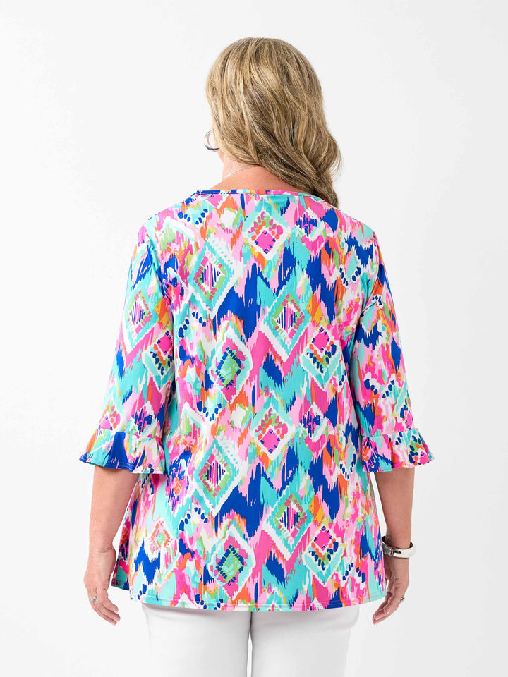 back view of a woman wearing a v-neck frill sleeve summer top with vibrant and playful print, paired with white pant