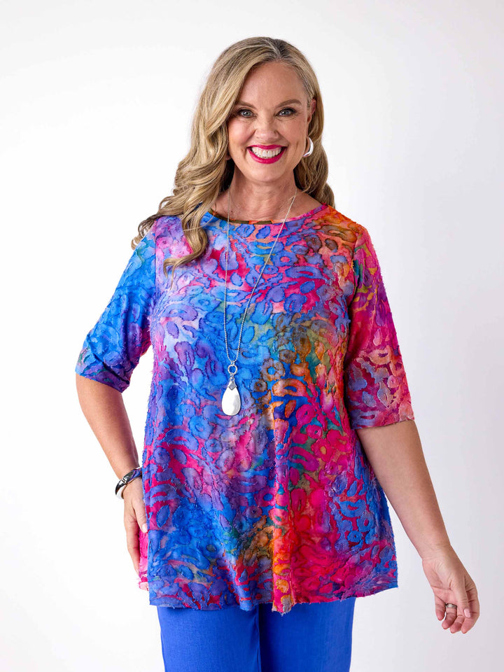 woman wearing a colourful swing jersey top with blue and pink tone print with burnout detail, paired with blue pants