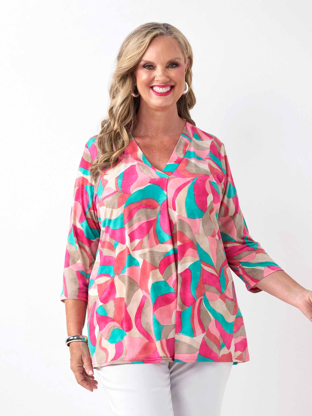 A woman wearing a colourful abstract print top in pink, with three-quarter sleeves and white pants