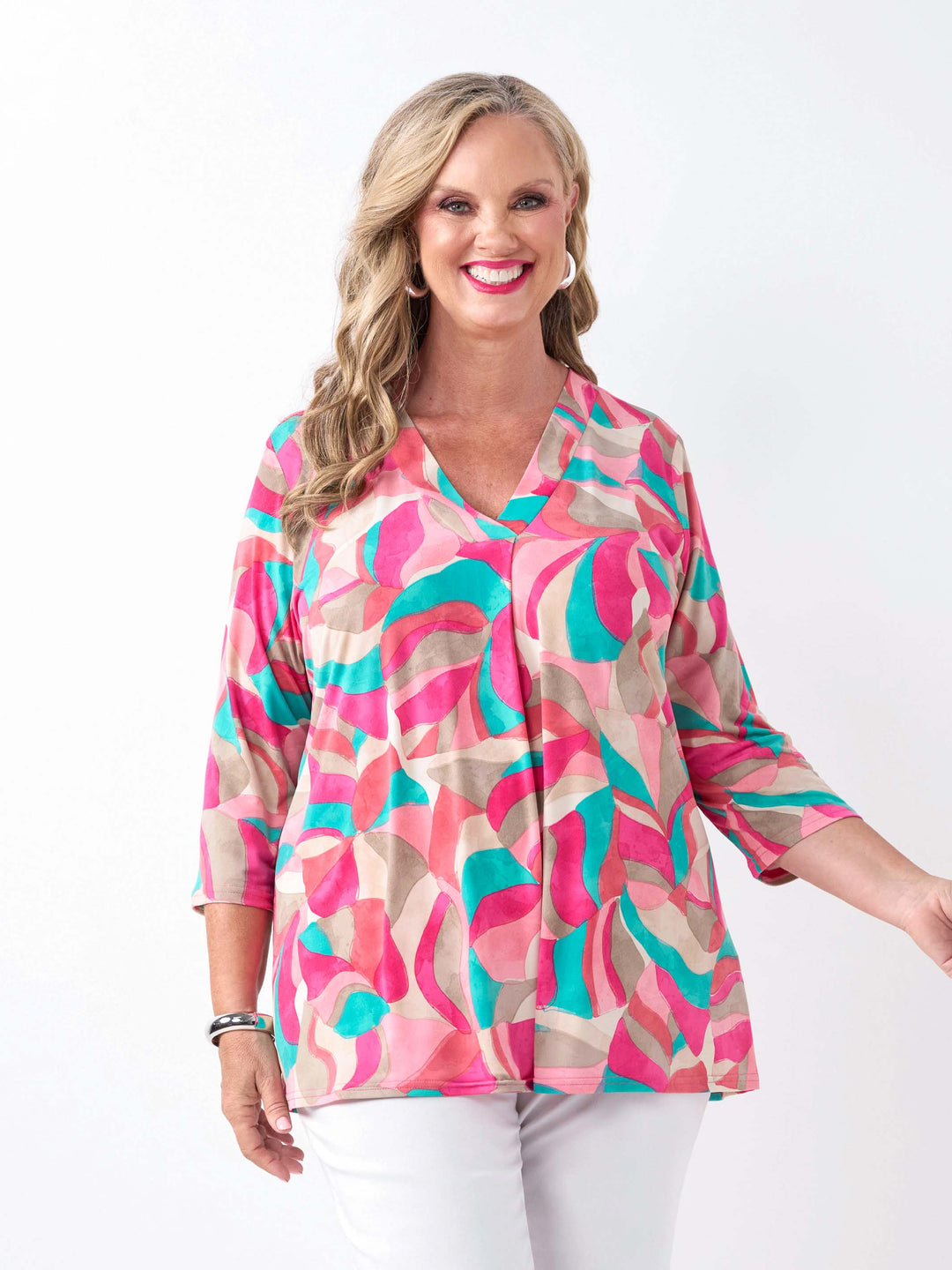 A woman wearing a colourful abstract print top in pink, with three-quarter sleeves and white pants