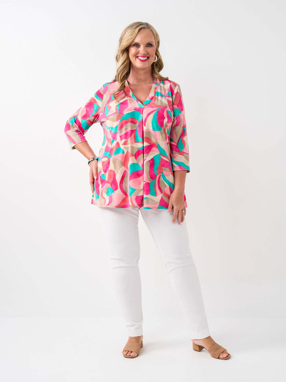 A woman wearing a colourful abstract print top in pink, with three-quarter sleeves and white pants