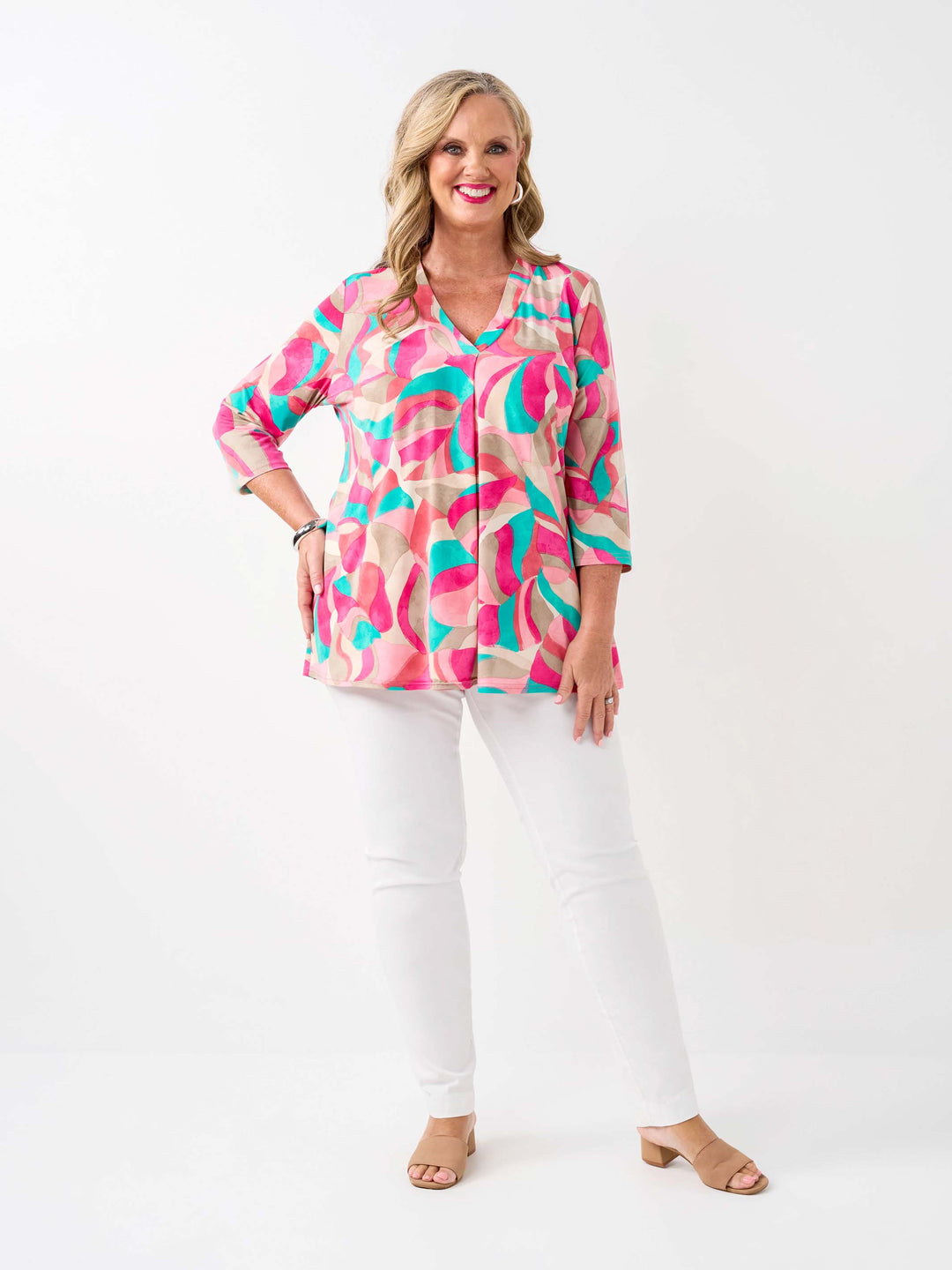 A woman wearing a colourful abstract print top in pink, with three-quarter sleeves and white pants