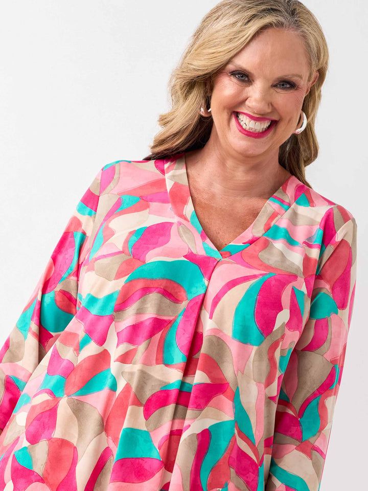 A woman wearing a colourful abstract print top in pink, with three-quarter sleeves and white pants