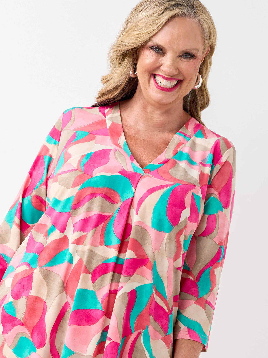 A woman wearing a colourful abstract print top in pink, with three-quarter sleeves and white pants