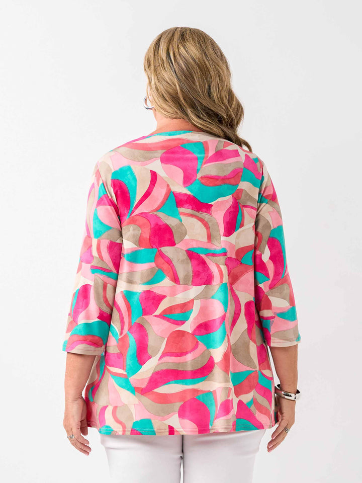 A back view of a woman wearing a colourful abstract print top in pink, with three-quarter sleeves and white pants