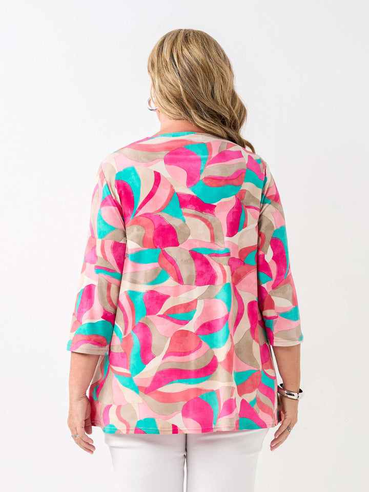 A back view of a woman wearing a colourful abstract print top in pink, with three-quarter sleeves and white pants