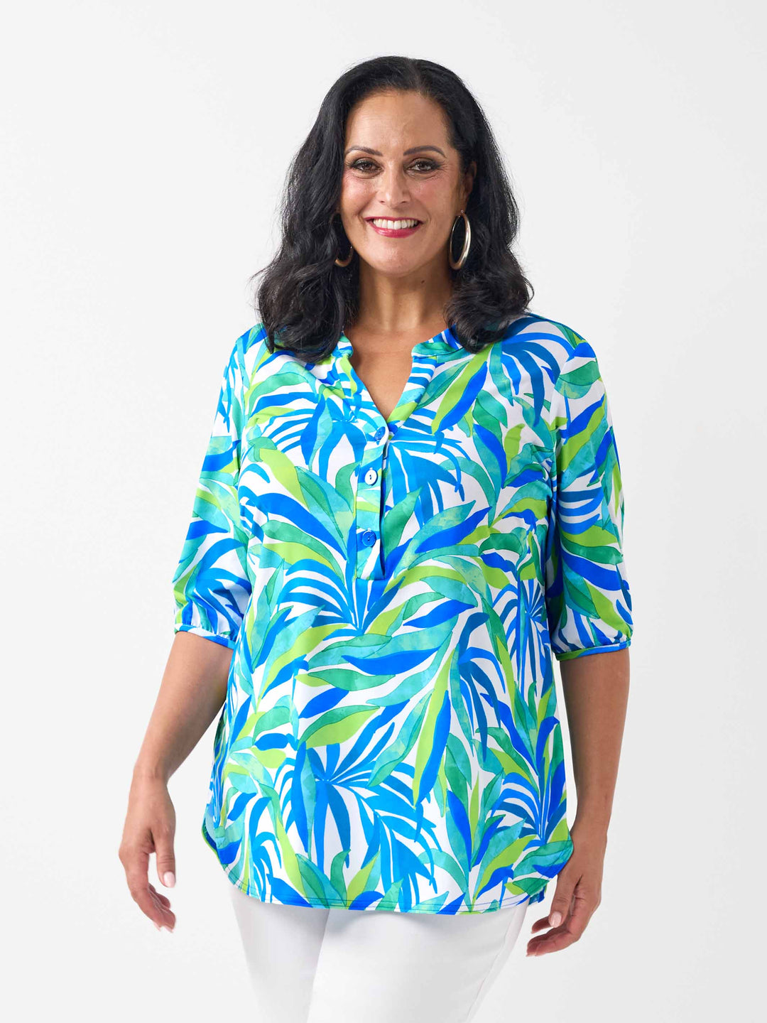 A woman wearing a three-quarter sleeve button-front blouse with a bold tropical leaf print in blue, green, and white