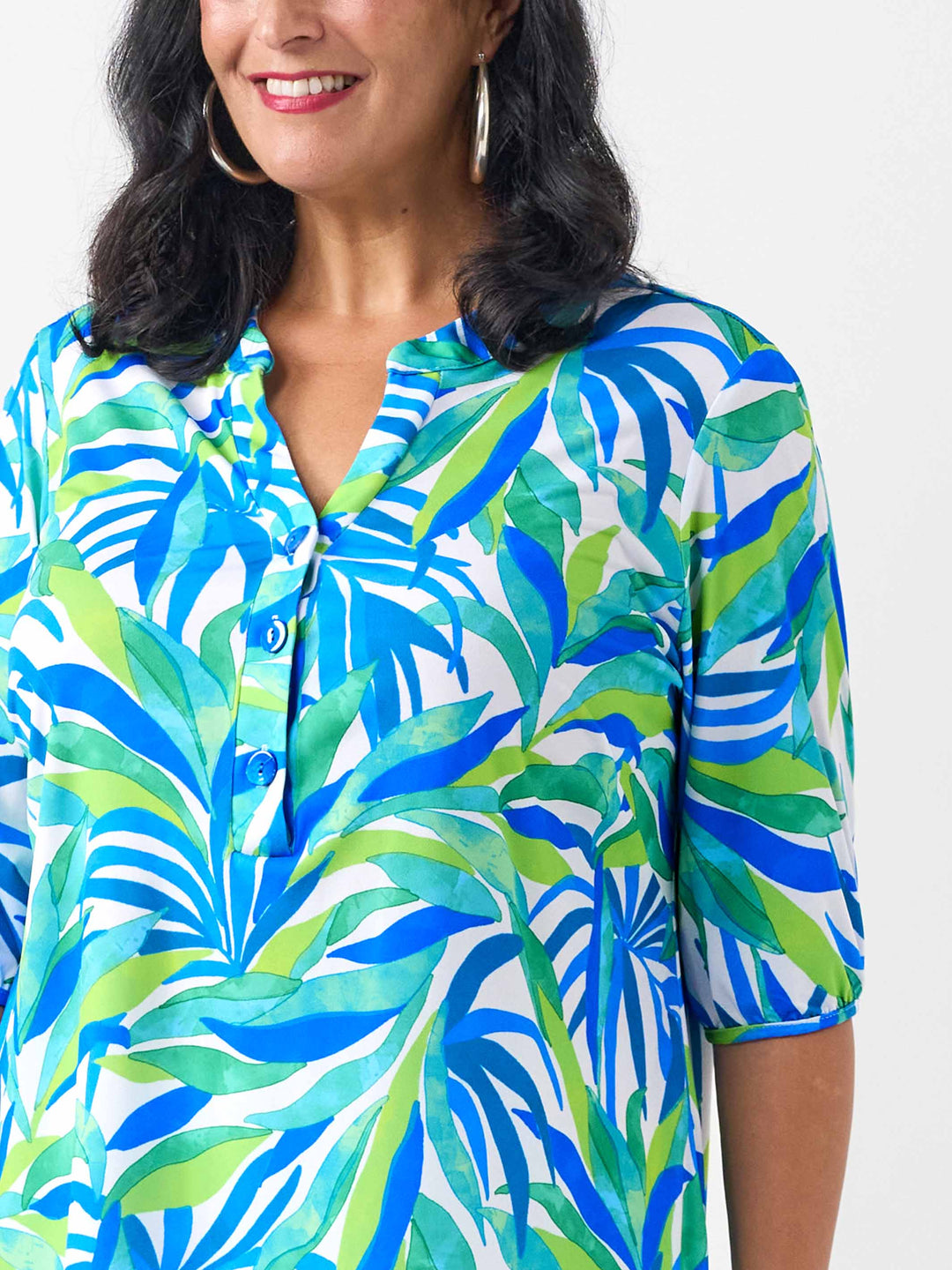 A woman wearing a short-sleeve button-front top with a bold tropical leaf print in blue, green, and white