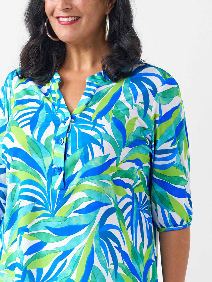 A woman wearing a short-sleeve button-front top with a bold tropical leaf print in blue, green, and white