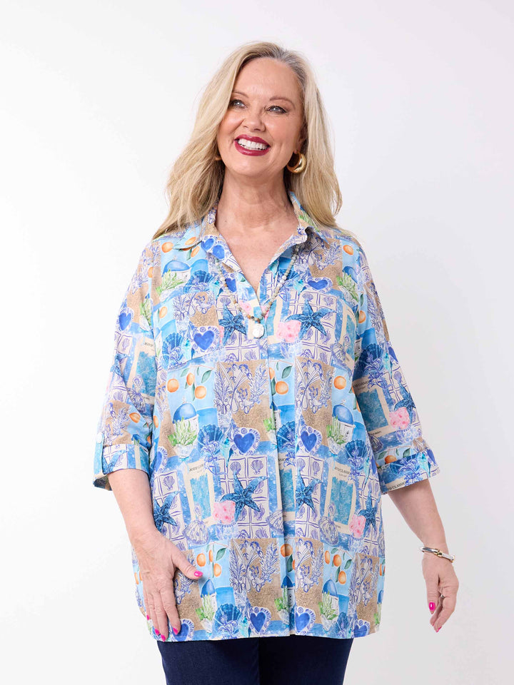 a woman wearing a collared cotton top with blue tropical resort print, featuring a three-quarter sleeves with tab details