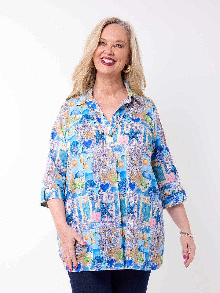 a woman wearing a collared cotton top with blue tropical resort print, featuring a three-quarter sleeves with tab details