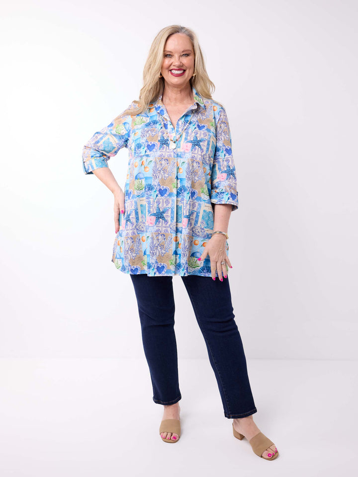 a woman wearing a collared cotton top with blue tropical resort print, featuring a three-quarter sleeves with tab details