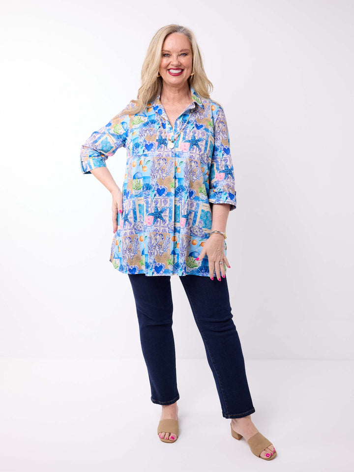 a woman wearing a collared cotton top with blue tropical resort print, featuring a three-quarter sleeves with tab details