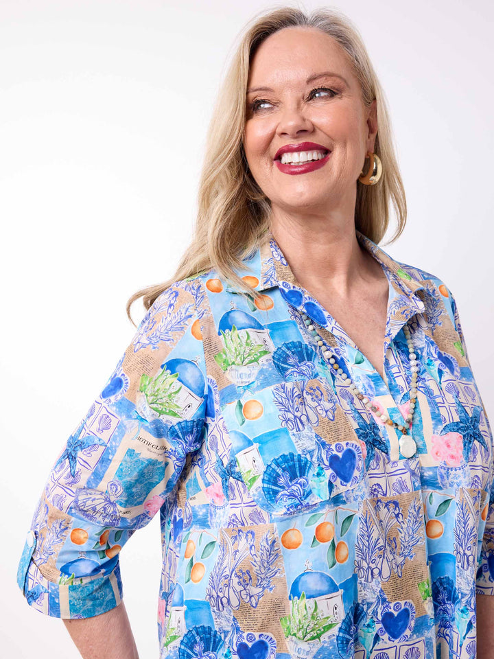 a woman wearing a collared cotton top with blue tropical resort print, featuring a three-quarter sleeves with tab details