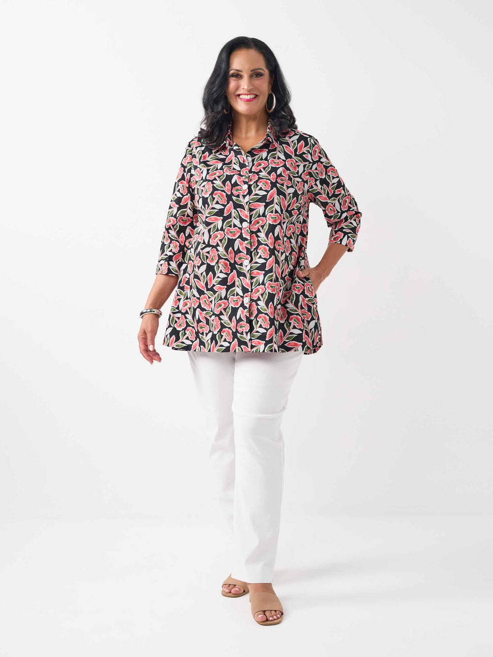 model wearing a button-up collared cotton shirt with a red and green floral print styled with white pant