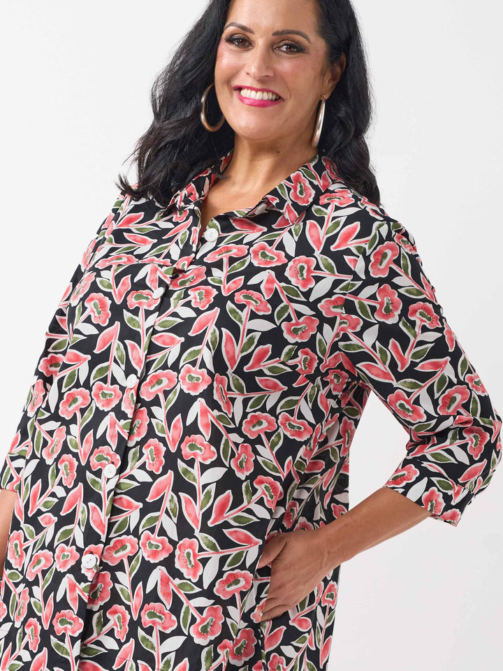 detail view of model wearing a button-up collared cotton shirt with a red and green floral print and side pockets