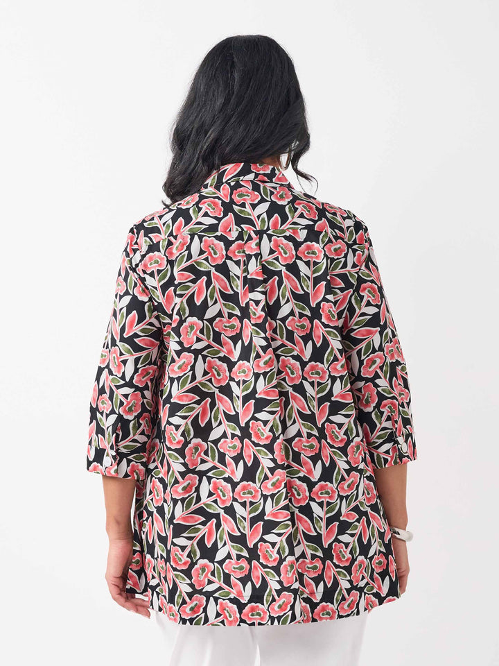 back view of model wearing a button-up collared cotton shirt with a red and green floral print