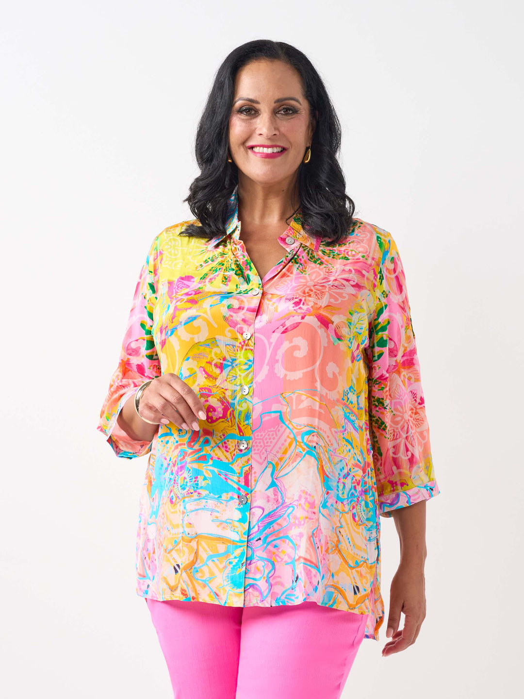 A woman waring a vibrant silky collared shirt with button front and colourful print in pink and yellow tone, paired with bright pink jeans