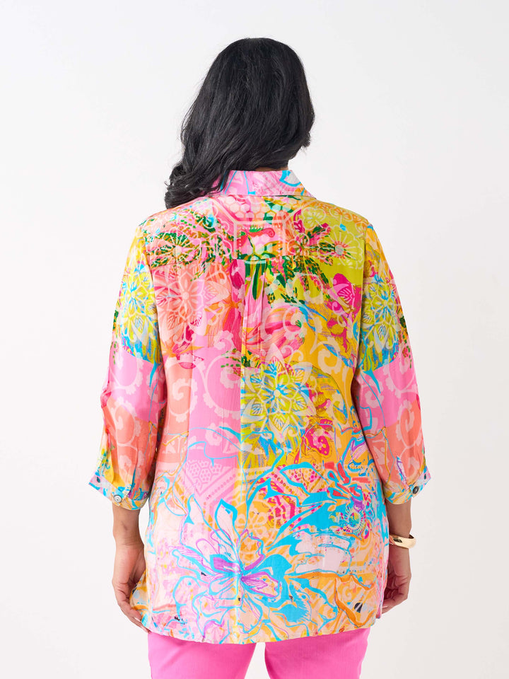 A woman viewed from the back waring a vibrant silky collared shirt with button front and colourful print in pink and yellow tone, paired with bright pink jeans