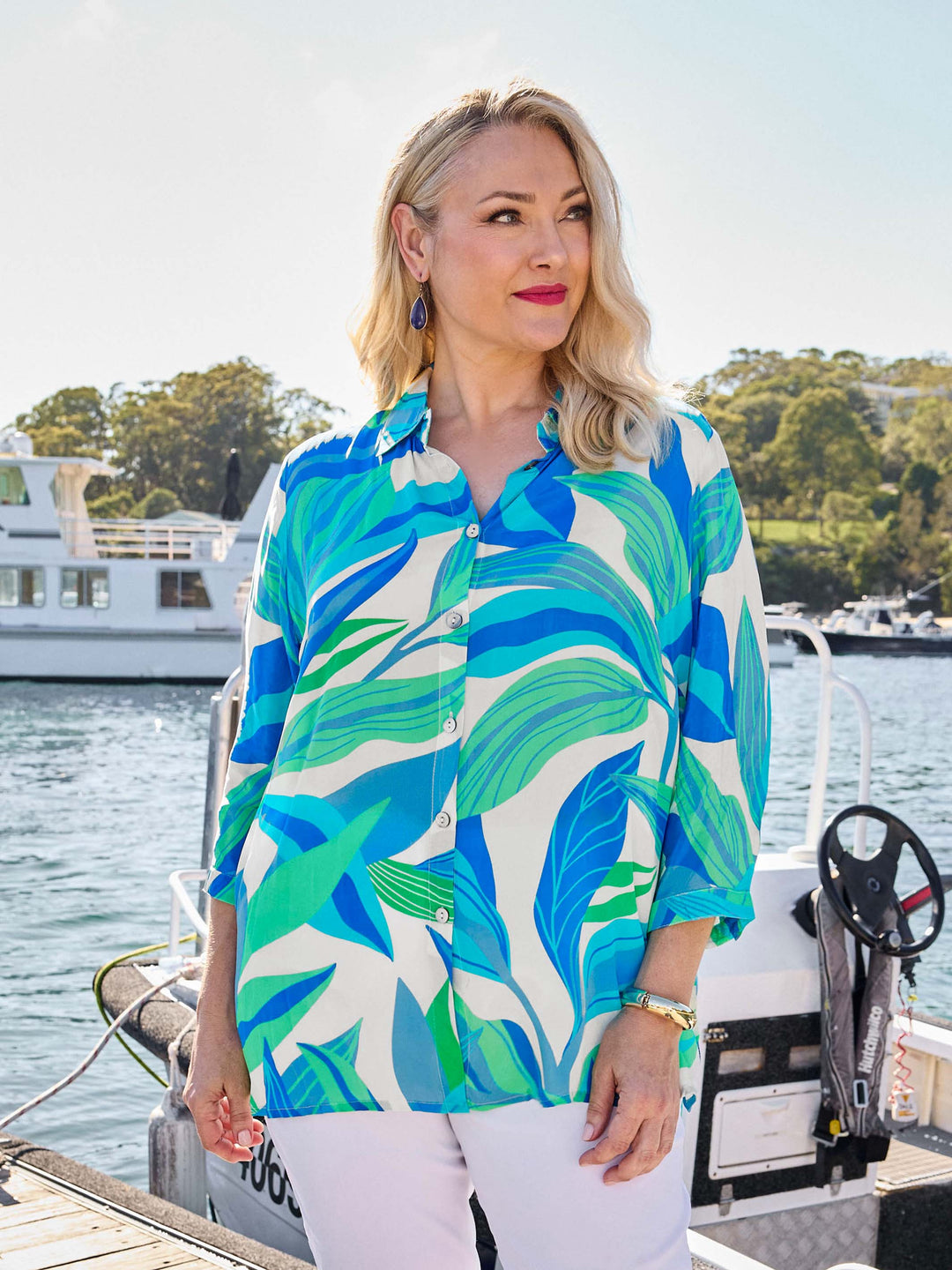 A woman wearing a silky collared shirt with aqua blue and green tropical leaves print