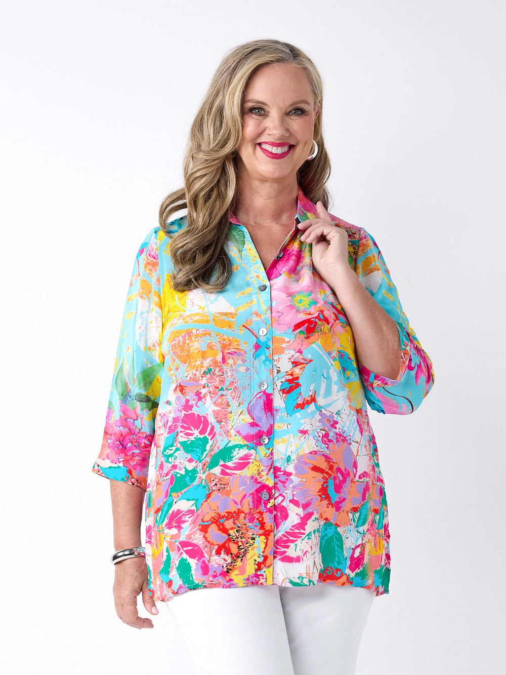 A woman wearing a vibrant abstract floral printed shirt in aqua blue and pink, paired with a pair of white pants