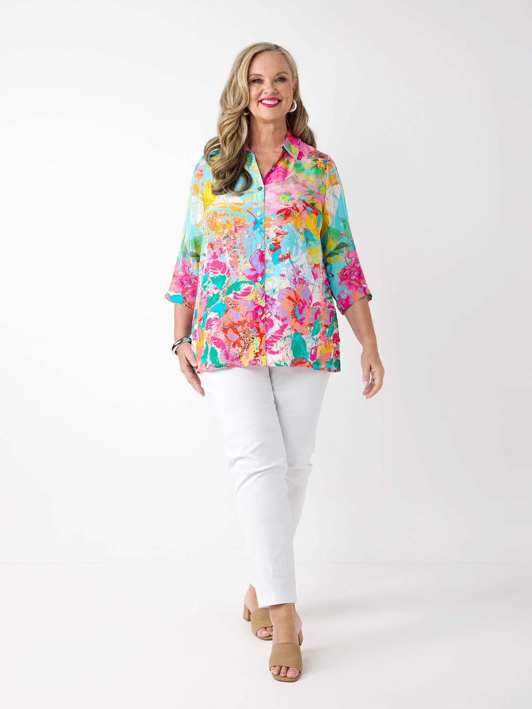 A woman wearing a vibrant abstract floral printed shirt in aqua blue and pink, paired with a pair of white pants