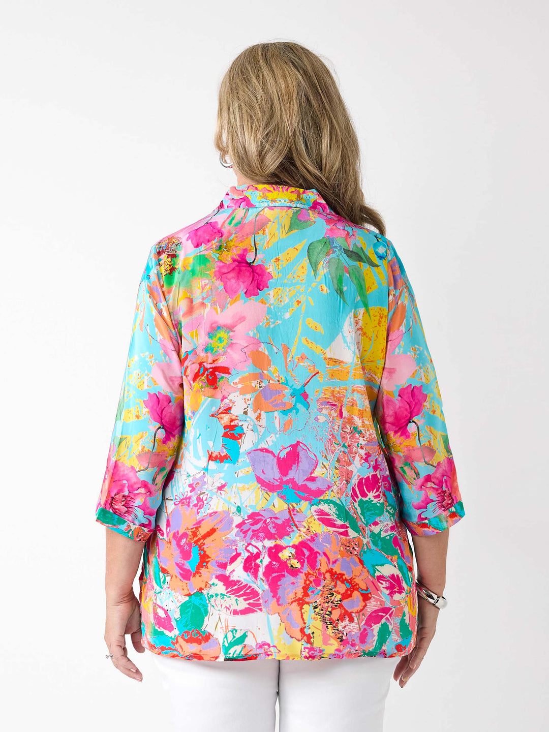 A woman wearing a vibrant abstract floral printed shirt in aqua blue and pink, paired with a pair of white pants
