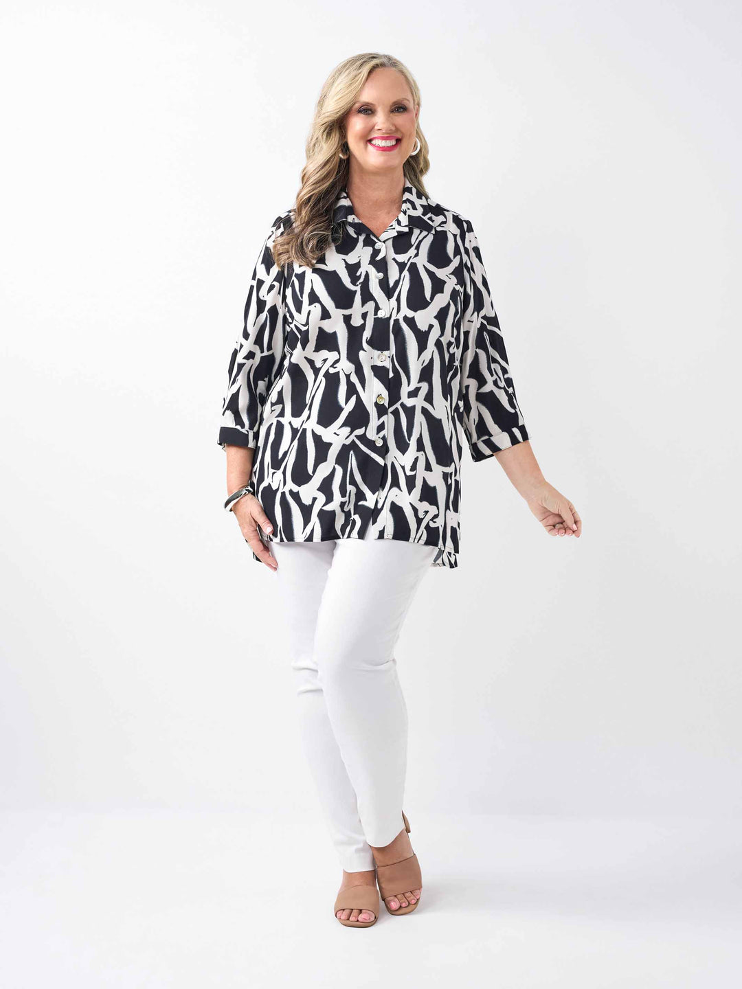 model wearing a black and white abstract printed button-up shirt with three-quarter sleeves and white pants