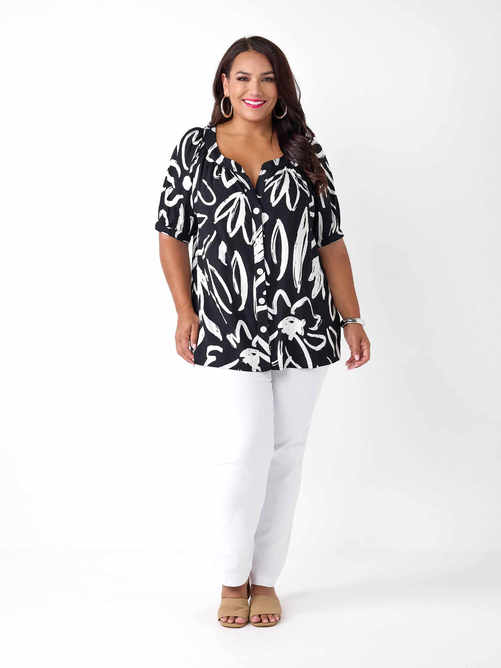 A woman wearing a black short-sleeve button-up blouse with a white abstract brushstroke print, paired with white pants
