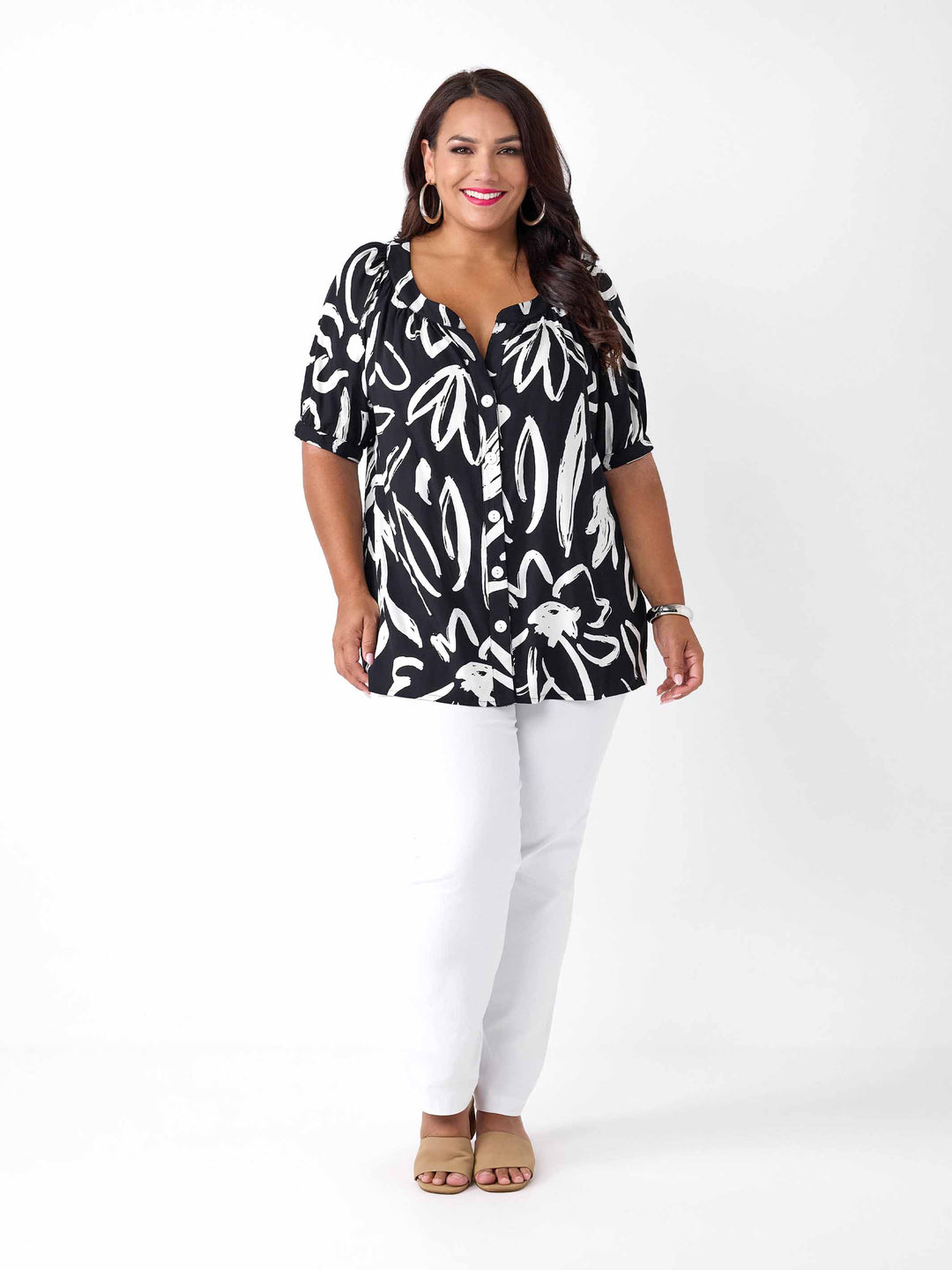 A woman wearing a black short-sleeve button-up blouse with a white abstract brushstroke print, paired with white pants