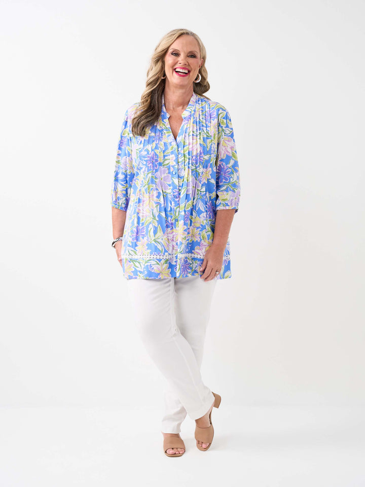 A woman wearing a blue floral printed button through top with pintuck detail at front and lace around the hem