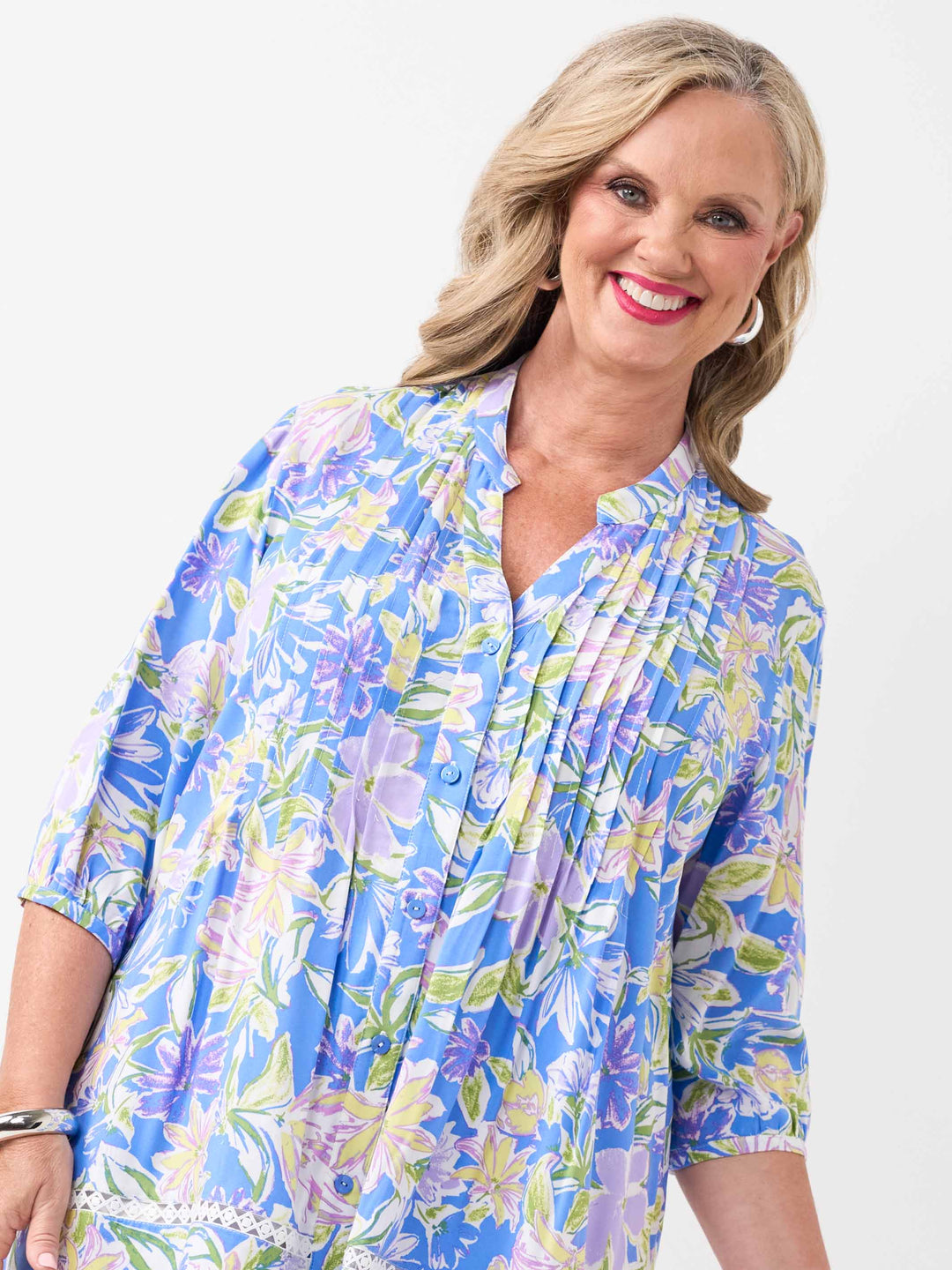A woman wearing a blue floral printed button through top with pintuck detail at front and lace around the hem