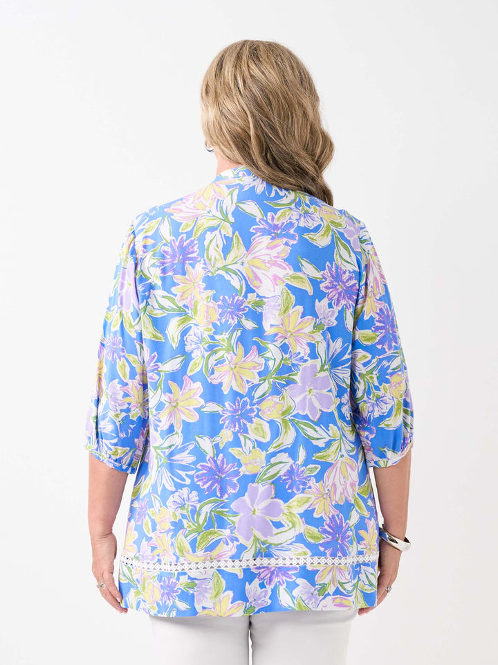 A woman wearing a blue floral printed button through top with pintuck detail at front and lace around the hem