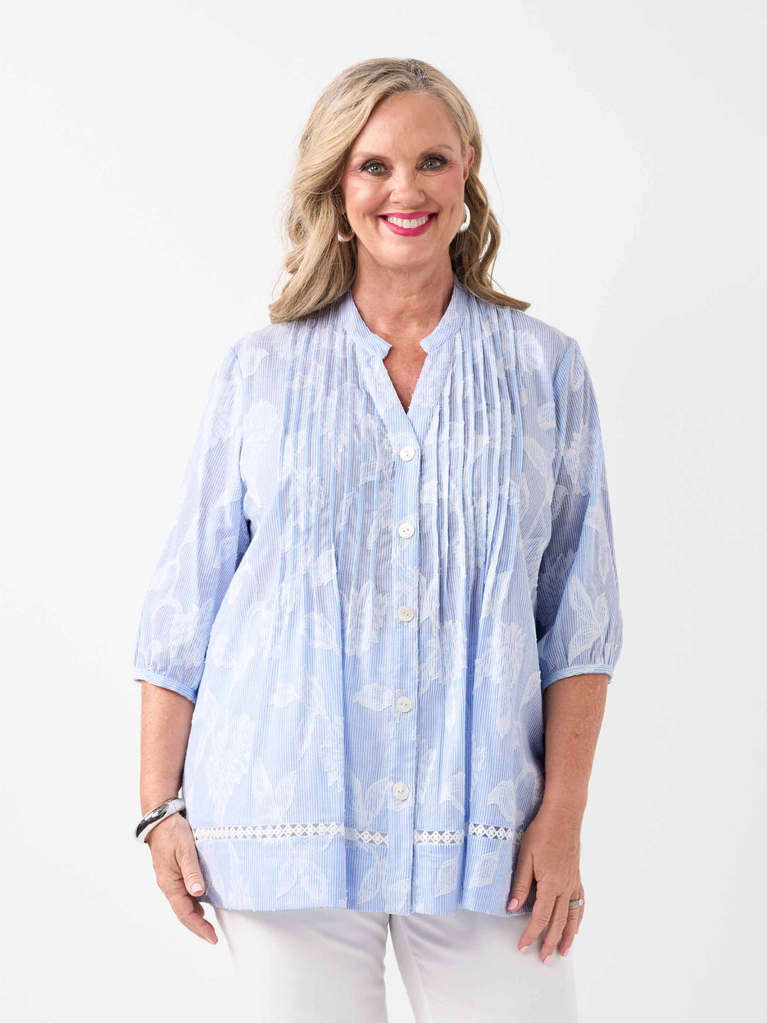 A  woman wearing a light blue and white patterned button-up blouse with pintuck detailing and white pants