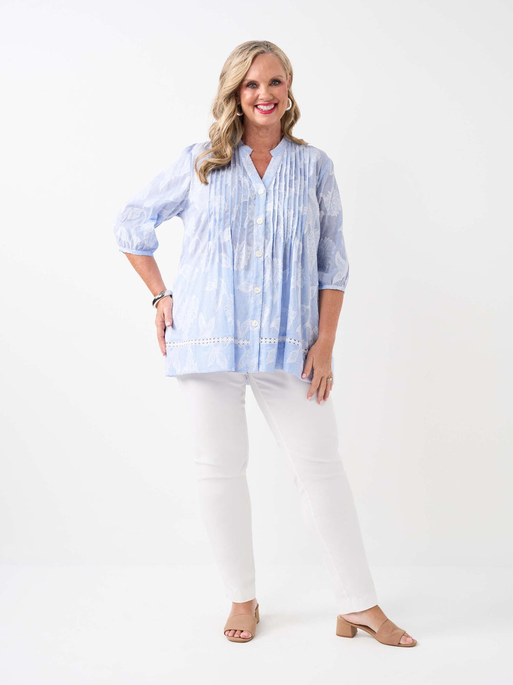 A  woman wearing a light blue and white patterned button-up blouse with pintuck detailing and white pants