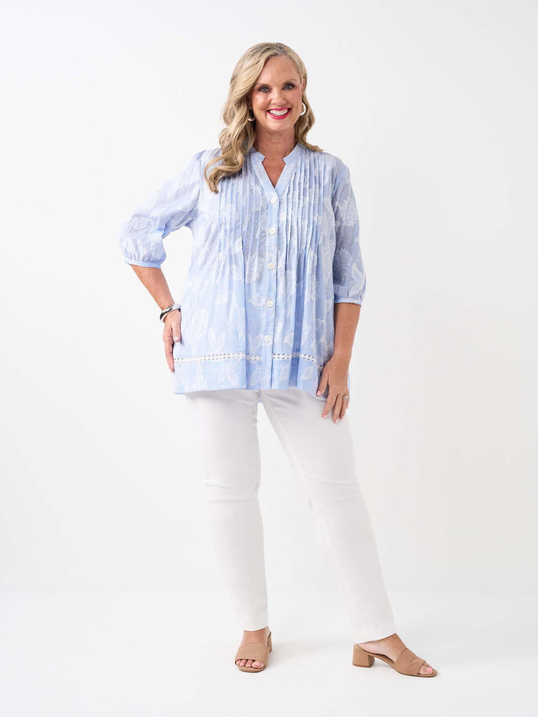 A  woman wearing a light blue and white patterned button-up blouse with pintuck detailing and white pants