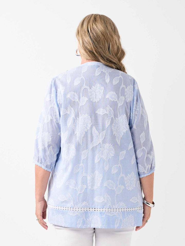 A woman viewed from the back wearing a ticking stripe shirt with white floral flocked design on a ticking stripe
