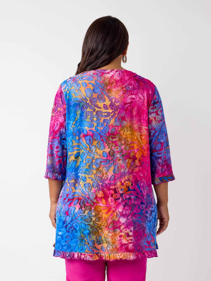 A woman viewed from the back wearing a vibrant, multicoloured floral burnout print tunic top with button through front and ruffle trim, paired with bright pink pants